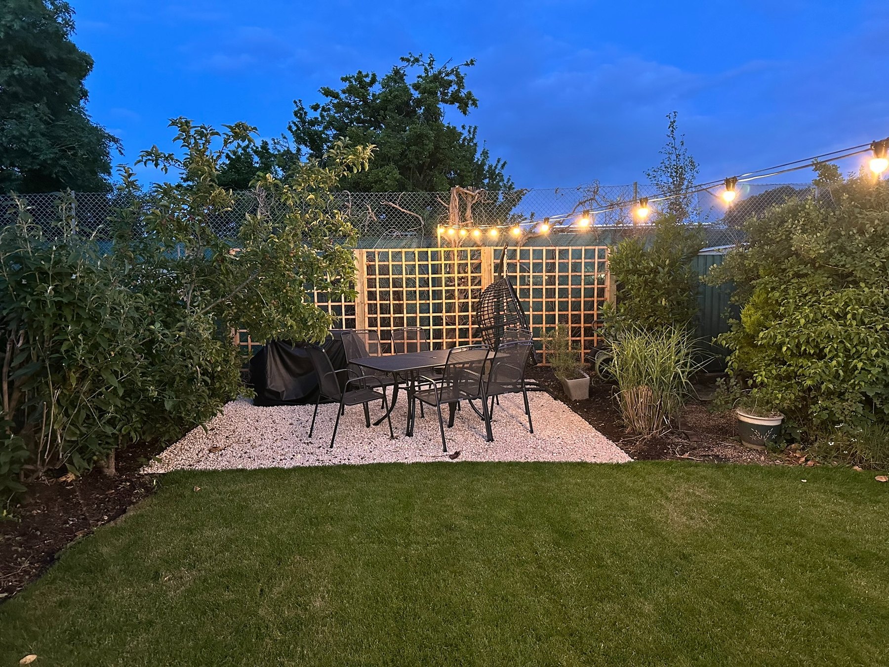 Gravel court outdoor dining area under warm festoon lights at dusk